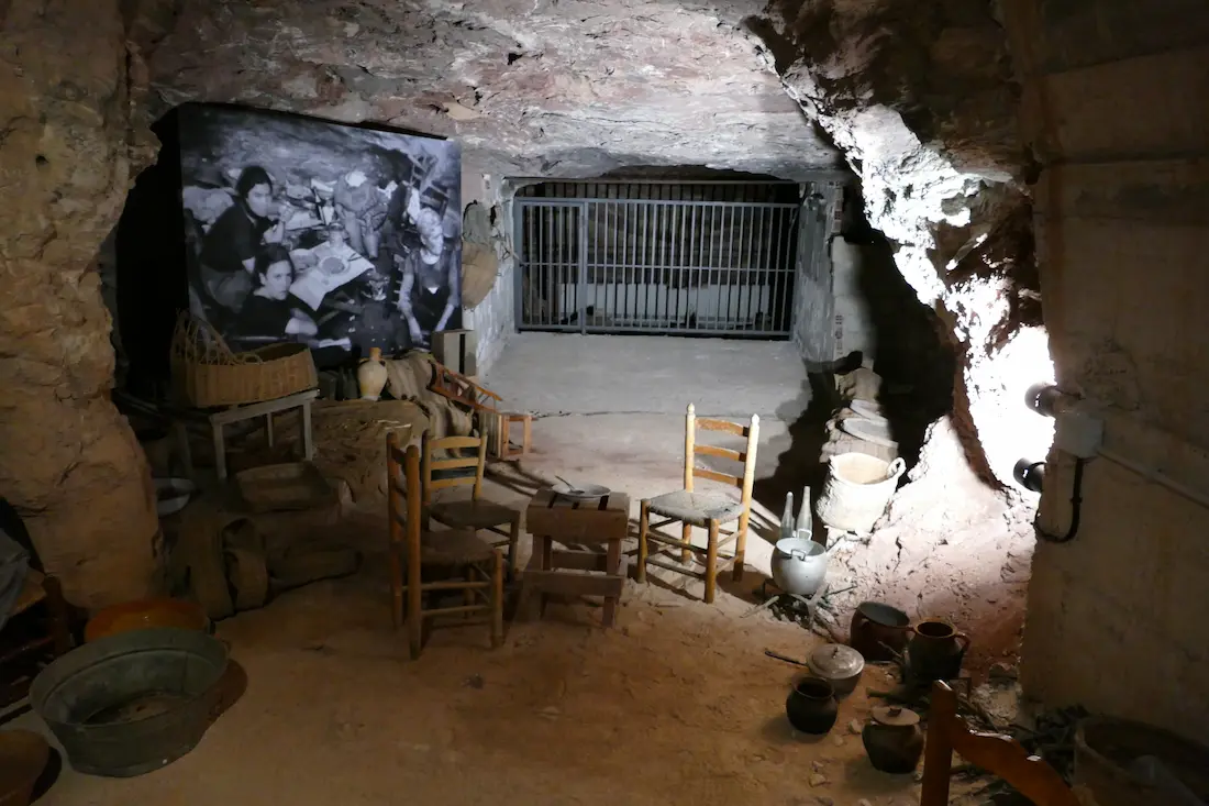 Ambientación de un refugio en el interior de la cueva, con mobiliario y enseres de las familias y una fotografía de época al fondo
