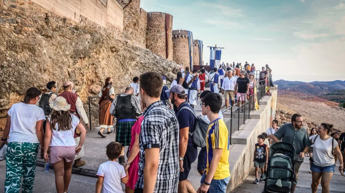 Visitantes y participantes disfrazados recorriendo el camino junto a la muralla del castillo de Onda durante la Feria Medieval