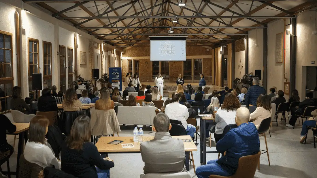 Interior de La Campaneta durante un evento nocturno en la nave principal, con el público sentado y pantalla de proyección