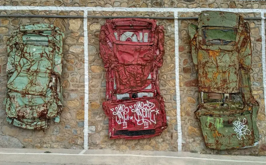 Instalación artística del MIAU de Fanzara: tres coches oxidados aplastados colgados en una pared de piedra como si fueran cuadros en una galería