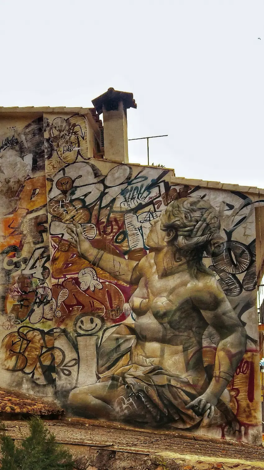 Mural del MIAU de Fanzara con figura humana clásica de gran escala sobre una fachada con capas de intervenciones artísticas superpuestas
