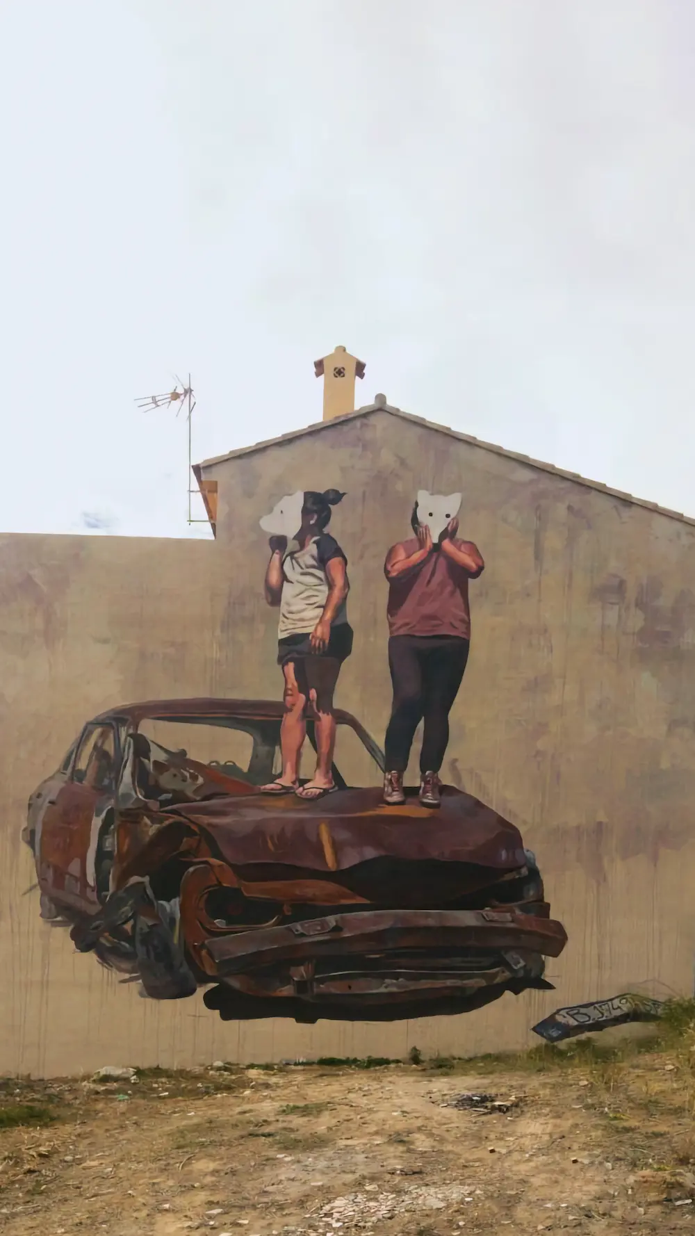 Mural de gran formato en el MIAU de Fanzara: dos figuras con máscaras de gato sobre un coche destrozado pintado en la fachada entera de un edificio