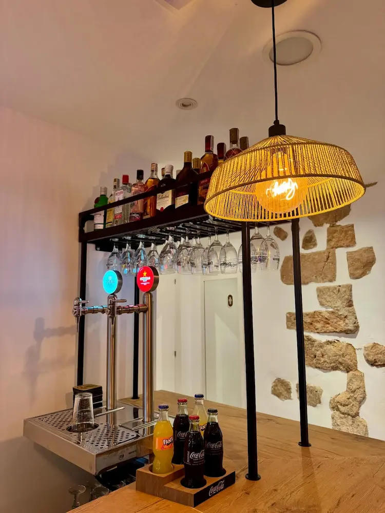 Barra de El Racó de Dins con tiradores de cerveza, copas colgadas y pared de piedra