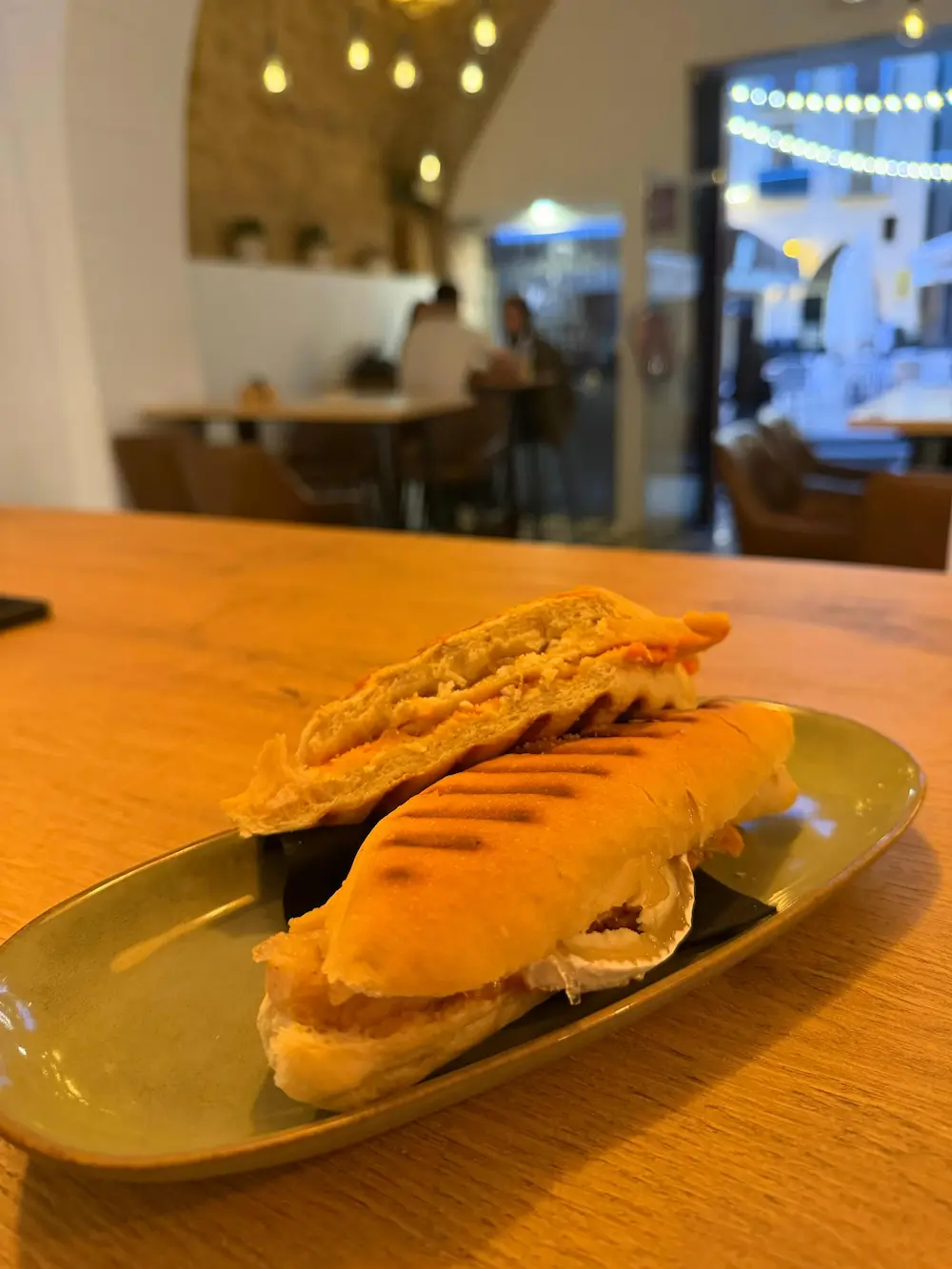 Planxada (bocadillo a la plancha) en primer plano con el interior del local al fondo, El Racó de Dins, Onda