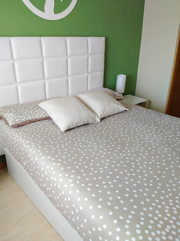 Cama hecha con sábanas de lunares beige sobre cabecero blanco acolchado