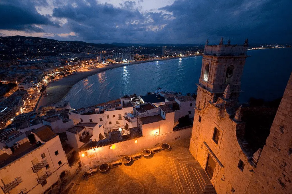 Vista nocturna de la ciudad vieja de Peñíscola desde el castillo del Papa Luna, con la Iglesia de Santa María en primer plano y la playa iluminada al fondo, Costa del Azahar